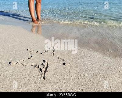 Rückansicht einer nicht erkennbaren Frau am Strand von Varadero, Kuba, die am Ufer in der Nähe eines Seesterns steht, der im Sand gezogen wird. Stockfoto