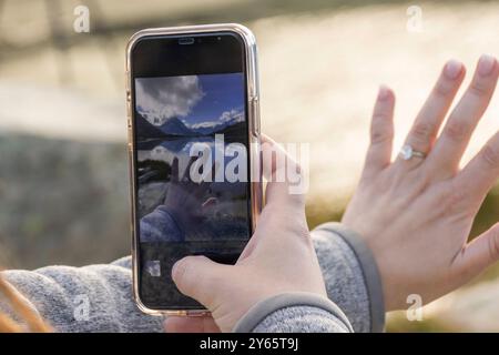 Eine beschnittene, nicht erkennbare Frau fängt ihren Verlobungsmoment in einem Foto ein und zeigt einen Verlobungsring und eine malerische Bergkulisse in einem Stockfoto