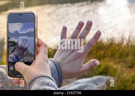 Eine beschnittene, nicht erkennbare Frau fängt ihren Verlobungsmoment in einem Foto ein und zeigt einen Verlobungsring und eine malerische Bergkulisse in einem Stockfoto