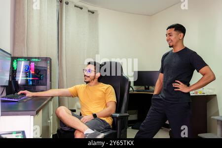 Ein fröhliches schwules Paar führt in seinem gemütlichen Home Office eine fröhliche Unterhaltung, ausgestattet mit moderner Technologie, ihre Ausdrucksformen spiegeln Glück und Glück wider Stockfoto