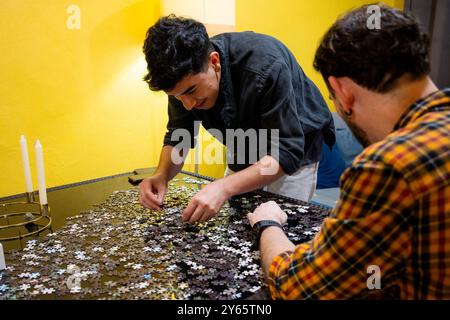 Ein junges schwules Paar konzentriert sich darauf, ein Puzzle in einem gemütlichen, warm beleuchteten Raum zusammenzustellen, um einen Moment der Verbundenheit und des gemeinsamen Interesses hervorzuheben Stockfoto