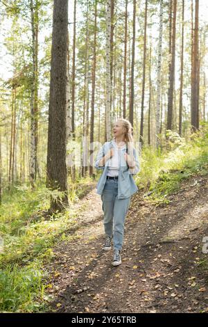 Eine Frau genießt einen angenehmen Spaziergang zwischen Birken in einem friedlichen Wald der freudige Moment wird festgehalten, während sie auf einem sonnendurchfluteten Waldweg spaziert Stockfoto