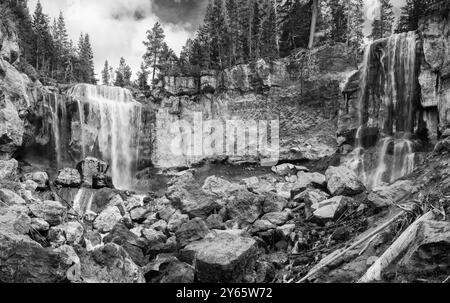 Ein Schwarzweiß-Foto, das einen Wasserfall in Newberry, National Volcanic Monument, Central Ore, über felsige Klippen fängt, umgeben von Wäldern Stockfoto