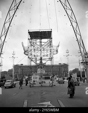 Die Mall bekommt diesen Krönungslook. Mit Menschenmassen auf den Gehwegen und Buckingham Palace als Rückwand heben die Arbeiter eine Nachbildung der Kronkoronette einer Prinzessin an , die an einem 65 Fuß langen Bogen hängen wird - einer von vier, die Teil der Krönungsdekoration in der Mall in London sein werden . Oben auf dem Bogen befinden sich ein Löwe und ein Einhorn in Stahlrohren . Mai 1953 Stockfoto