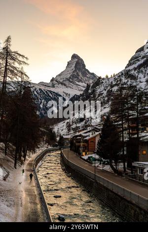 Atemberaubende Winterszene mit dem majestätischen Matterhorn in der Schweiz im Hintergrund, mit einem ruhigen Fluss und einer typischen alpinen Architektur Stockfoto