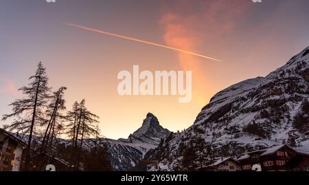 Der majestätische Gipfel des Matterhorns unter dem Abendhimmel in der Schweiz, der seine Silhouette vor einem lebhaften Hintergrund projiziert, der von einem orangen Farbton beleuchtet wird Stockfoto