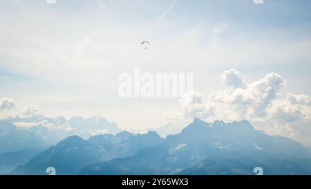 Ein atemberaubender Blick auf die Schweizer Alpen unter klarem Himmel, mit einem weit entfernten Gleitschirmflieger und geschwollenen Wolken Stockfoto