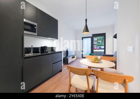 Ein gut eingerichtetes, modernes Ferienapartment mit elegantem Küchendesign, das nahtlos in einen hellen Essbereich mit Holztisch und m mündet Stockfoto