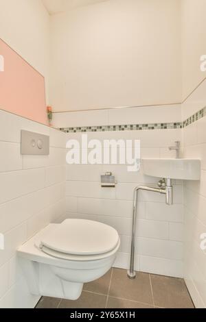Modernes Bad mit weißer Toilette, Waschbecken und gefliesten Wänden mit grauen Mosaikfliesen. Stockfoto