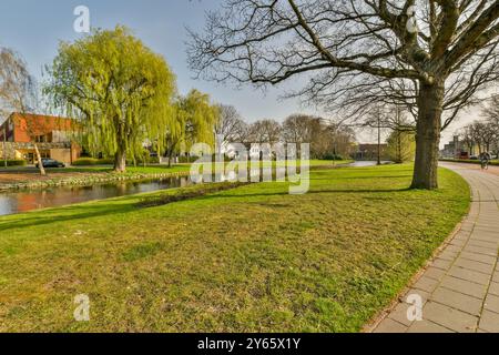 Ein ruhiger Park mit weinenden Weiden und einem ruhigen Teich an einem sonnigen Tag, mit einem gepflasterten Weg und üppigem Gras. Stockfoto