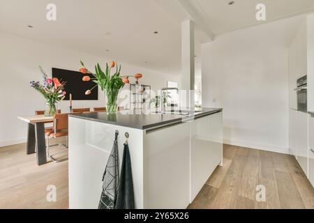 Eine helle und geräumige Küche mit eleganten weißen Schränken führt in einen Essbereich mit Holztisch, Ledersesseln und frischen Blumen. Stockfoto