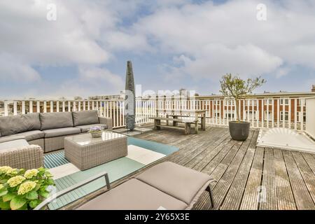 Elegante Dachterrasse mit modernen Gartenmöbeln, gemütlichem Lounge-Set und Holzfußboden vor städtischem Hintergrund Stockfoto