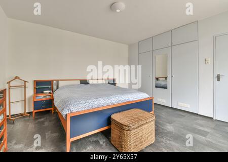 Ein gut beleuchtetes, modernes Schlafzimmer mit einem großen Bett mit marineblauer Verkleidung, passenden Holzmöbeln und einer sauberen, minimalistischen Ästhetik. Stockfoto