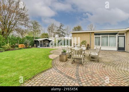 Ein ruhiger Hinterhof mit einer gepflasterten Terrasse, Holzgartenmöbeln, üppigem Rasen und einem charmanten Gartenschuppen, umgeben von Grün. Stockfoto