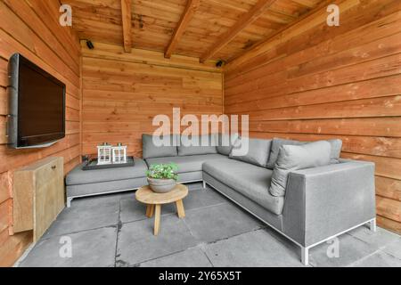 Moderner Innenhof mit einem weichen grauen Sofa, rundem Holztisch und elegantem, an der Wand montiertem Fernseher, der in einem warmen Raum untergebracht ist Stockfoto