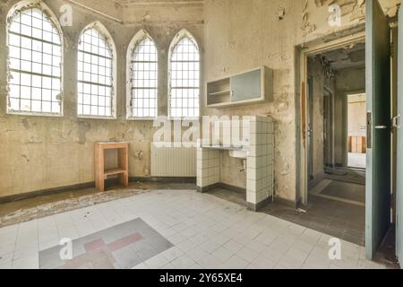 Ein Blick von innen auf einen baufälligen und leeren Raum mit Bogenfenstern, Risswänden und einem gefliesten Boden. Stockfoto