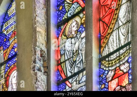 Ein lebhaftes Buntglasfenster mit einem Engel, beleuchtet und detailliert vor einer historischen Kirche. Stockfoto