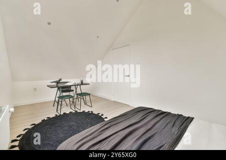 Ein gemütliches Schlafzimmer im Dachgeschoss mit minimalistischem Design, kleinem Schreibtisch mit zwei Stühlen, einem komfortablen Bett und eleganter Einrichtung. Stockfoto