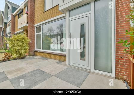 Ein moderner Hauseingang mit einer großen Glastür und einem gefliesten Gang, ergänzt durch einen üppig grünen Sträucher. Stockfoto