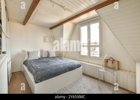 Helles Schlafzimmer im Dachgeschoss mit Doppelbett, weißer Täfelung und Dachfenster. Stockfoto