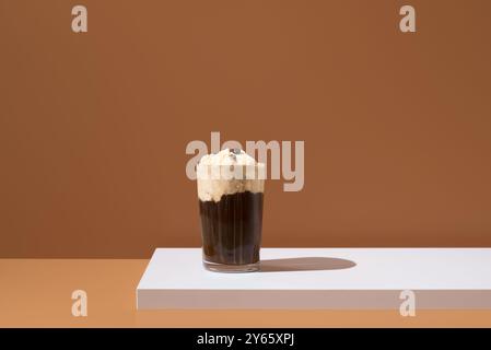 Ein elegantes Affogato-Dessert mit einer Schaufel Vanilleeis, getränkt in kräftigem Kaffee, präsentiert auf einer sauberen weißen Oberfläche mit warmbraunem Hintergrund Stockfoto
