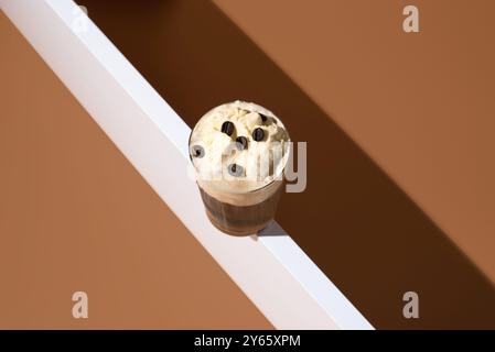 Blick von oben auf köstliches Affogato mit reichhaltigem Espresso, gekrönt mit cremigem Vanilleeis und Kaffeebohnen, auf minimalistischem beigem Hintergrund. Stockfoto