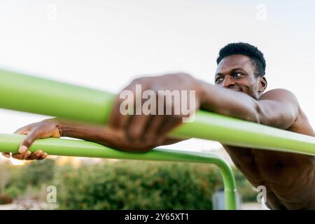 Ein fokussierter junger Mann macht sich mit Calisthenics beschäftigt, indem er an einer grünen Bar in einem Outdoor-Park Pull-ups macht und Stärke und Entschlossenheit zeigt Stockfoto