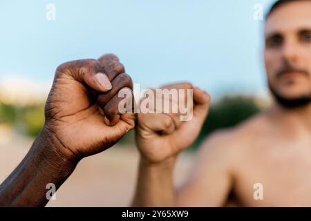 Zwei Freunde stoßen mit Fäusten an, um Solidarität und Motivation zu zeigen, während sie sich von einer Calisthenics-Session im Freien ausruhen Stockfoto