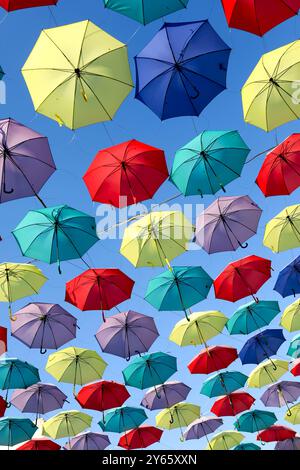 Bunte Regenschirme schweben ruhig in einem hellblauen Himmel und schaffen ein fröhliches und künstlerisches Überdachungsdach Stockfoto