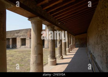 Ein ruhiger Innenhof mit alten, verwitterten Säulen und verblassten Fresken erinnert an den historischen Charme von Pompeji, das durch Holzbalken behinderte Sonnenlicht Stockfoto