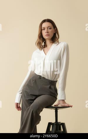 Weibliches Modell mit weißer Bluse und maßgeschneiderter grauer Hose. Klassischer Business-Look. Studio-Aufnahme. Stockfoto