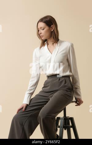 Weibliches Modell mit weißer Bluse und maßgeschneiderter grauer Hose. Klassischer Business-Look. Studio-Aufnahme. Stockfoto