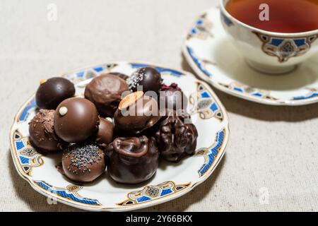 Auswahl an fein gefüllten Schokoladenbonbons auf einem Teller mit einer Tasse rotem Tee. Stockfoto