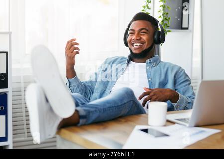 Fröhlicher Mitarbeiter, der sich am Arbeitsplatz entspannt, Musik hört und virtuelle Gitarre spielt Stockfoto