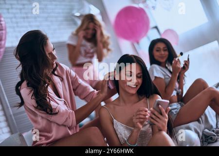 Welche Frisur willst du? Vier attraktive junge Frauen im Pyjama lächeln während der Schönheitsbehandlung im Schlafzimmer Stockfoto