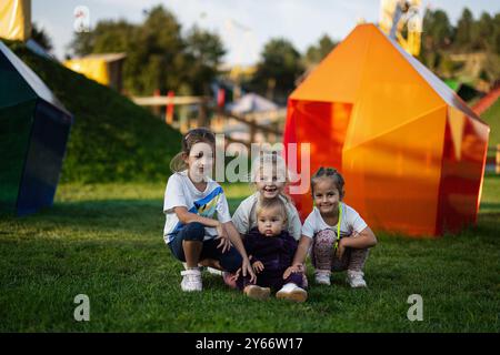 Eine lebhafte Gruppe von vier Kindern genießt einen sonnigen Tag in einem farbenfrohen Park. Die Kinder lächeln und haben Spaß, auf dem Gras zu sitzen, umgeben von vibra Stockfoto