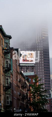 Das Bild zeigt eine urbane Stadtlandschaft, in der die Spitze eines hohen modernen Gebäudes von dickem Nebel verdeckt wird. Stockfoto