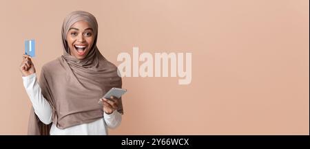 Überglücklich Black Muslim Girl In Hijab Holding Kreditkarte Und Smartphone Stockfoto