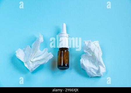 Nasenspray für laufende Nase und zerknitterte Papiertücher auf blauem Hintergrund. Erkältungszeit und Krankheitszeit Stockfoto