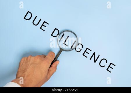 Eine Hand, die eine Lupe über die Worte „DUE DILIGENCE“ auf blauem Hintergrund hält. Wirtschaft, Finanzen, Recht, Forschungskonzept. Stockfoto