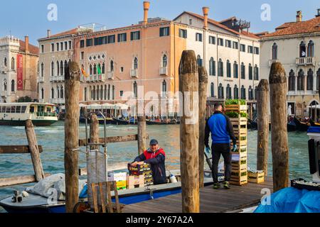 Zwei Männer entladen auf einer Anlegestelle am Canale Grande im San Polo Sestiere von Venedig, Italien, Kisten mit Obst und Gemüse Stockfoto