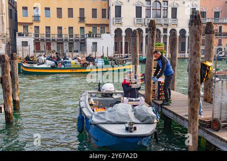 Zwei Männer entladen auf einer Anlegestelle am Canale Grande im San Polo Sestiere von Venedig, Italien, Kisten mit Obst und Gemüse Stockfoto