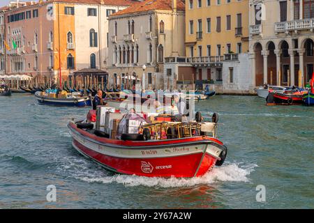 Ein motorisiertes Handelsboot, das mit Waren beladen ist, fährt entlang des Canal Grande in Venedig, Italien Stockfoto