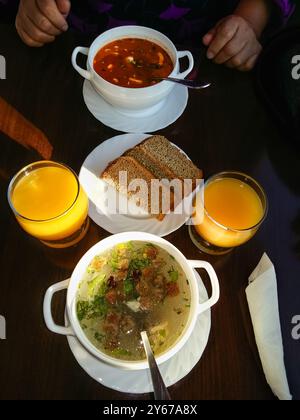 Pilzsuppe in weißen Schüsseln dunkles Brot und frischer Orangensaft auf rustikalem Holztisch. Draufsicht. Eine Frau, die bereit ist, ihr Mittagessen zu essen. Knochenbrühe aus Stockfoto