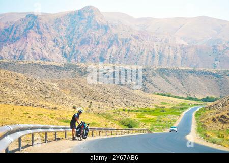 Männliche Radfahrer mit Tourenfahrrad in den Bergen am Straßenrand haben Pausen-Pause. Alleinreise mit Fahrradtaschen. Langzeitreisen Stockfoto