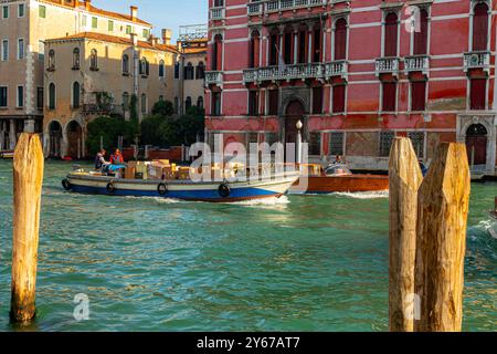 Ein motorisiertes Handelsboot mit Waren und einem Wassertaxi auf dem Canal Grande in Venedig, Italien Stockfoto