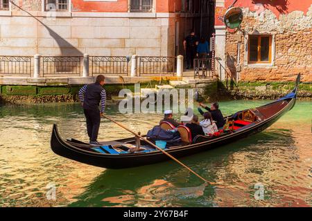 Menschen genießen eine Gondelfahrt, während der Gondoliere seine Gondelbahn entlang des Rio del Palazzo, einem Kanal im Castello Sestiere von Venedig, Italien, fährt Stockfoto