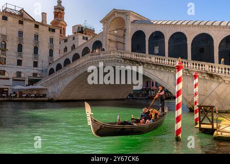 Ein Paar, das eine Gondelfahrt macht, während der Gondoliere seine Gondelbahn entlang des Canal Grande in der Nähe der Rialto-Brücke in Venedig, Italien, steuert Stockfoto