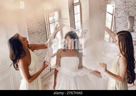 Genießen Sie die Hochzeitsvorbereitungen. Blick von oben auf die Brautjungfern, die der Braut helfen, sich einen Schleier anzulegen und lächelnd in der Garderobe zu stehen Stockfoto