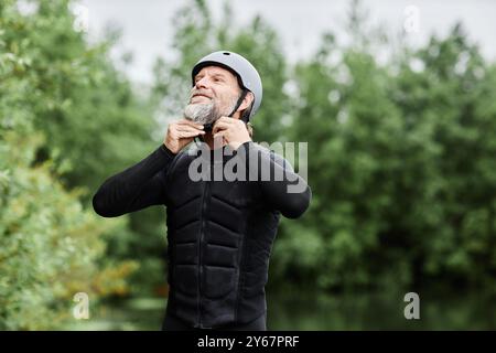 Porträt eines bärtigen älteren Mannes, der Taucheranzug und Helm anzieht und bereit ist, Wassersport am See im Wald zu genießen Stockfoto